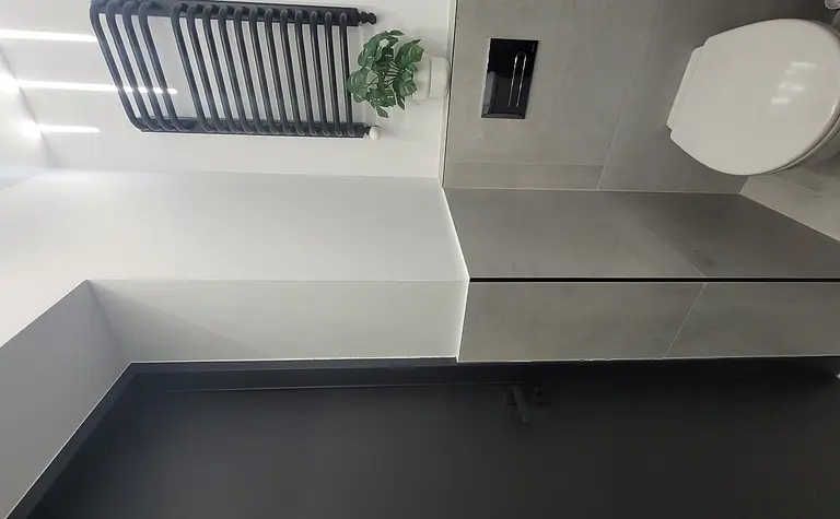 Toaleta w stylu minimalistycznym z szarymi płytkami, czarnymi akcentami i rośliną.