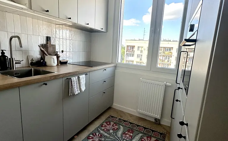 Kuchnia w stylu boho, eklektycznym i skandynawskim z szarymi meblami i kolorowym dywanem.