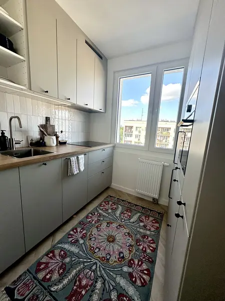 Kuchnia w stylu boho, eklektycznym i skandynawskim z szarymi meblami i kolorowym dywanem.