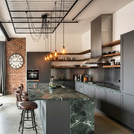 Kuchnia industrialna z ciemnym blatem, ceglaną ścianą i wiszącymi lampami.