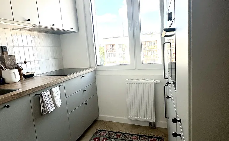 Kuchnia w stylu boho, eklektycznym i skandynawskim z szarymi meblami i kolorowym dywanem.