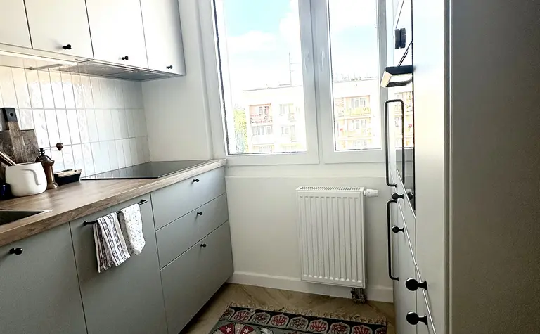 Kuchnia w stylu boho, eklektycznym i skandynawskim z szarymi meblami i kolorowym dywanem.