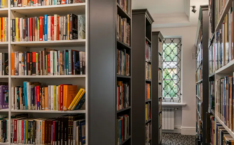 Wnętrze biblioteki z dużymi regałami, tradycyjny styl, książki na półkach, wygodne miejsce do czytania.