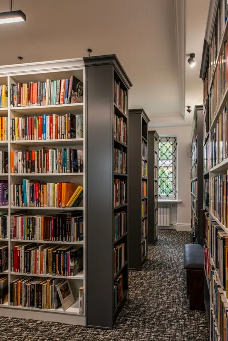 Wnętrze biblioteki z dużymi regałami, tradycyjny styl, książki na półkach, wygodne miejsce do czytania.