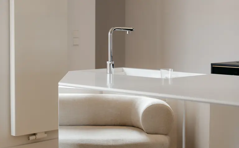 Wnętrze kuchni z białym blatem, beżowym fotelem oraz minimalistycznymi akcentami.