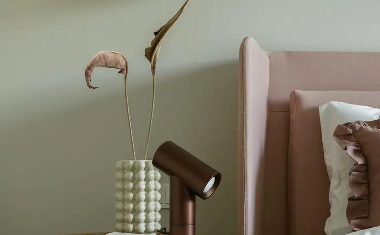 Sypialnia w stylu nowoczesnym z różowym łóżkiem, minimalistycznymi dodatkami i lampą.