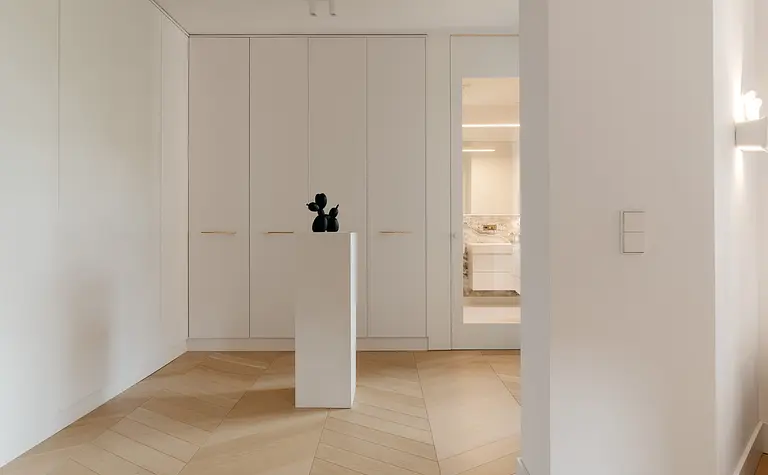 Garderoba w stylu minimalistycznym z białymi meblami i akcentami w kolorze drewna.