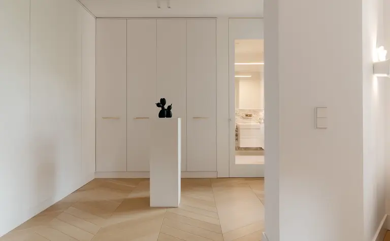 Garderoba w stylu minimalistycznym z białymi meblami i akcentami w kolorze drewna.