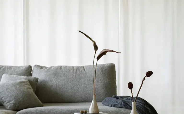 Wnętrze salonu z szarym narożnikiem i minimalistycznymi dekoracjami w stylu quiet luxury.
