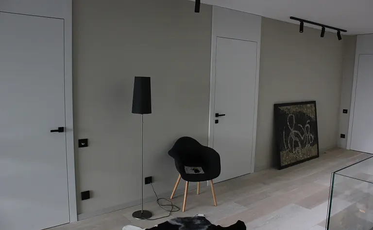 Minimalistyczne wnętrze z czarną lampą, białymi drzwiami i nowoczesnym wystrojem.