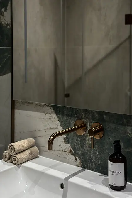 Wnętrze łazienki z umywalką, marmurowymi płytkami, złotym kranem i ręcznikami.