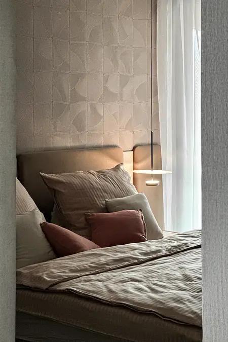 Wnętrze sypialni z beżowym łóżkiem, poduszkami i szarym tłem.