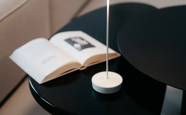 Eklektyczne wnętrze z minimalistycznym stolikiem, lampą i książką.