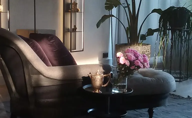 Wnętrze eklektycznego salonu z szarym fotelem, roślinami i dekoracjami.