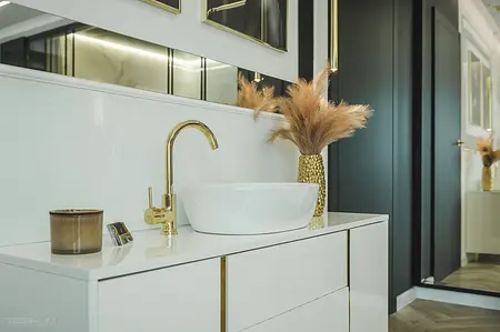 Nowoczesna łazienka z białą umywalką, złotym kranem i dekoracjami w stylu glamour.
