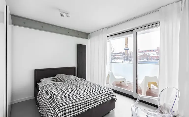 Sypialnia w stylu industrialnym i minimalistycznym z dużymi oknami i nowoczesnym łóżkiem.