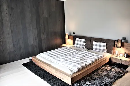 Minimalistyczna sypialnia z drewnianym łóżkiem, szarymi ścianami i nowoczesnym oświetleniem.