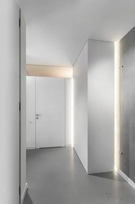 Wnętrze przedpokoju w stylu industrialnym i minimalistycznym z białymi ścianami i szarym podłogą.