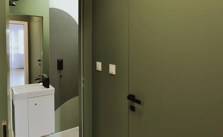Minimalistyczny przedpokój z zielonymi ścianami, białą umywalką i czarnymi akcentami.