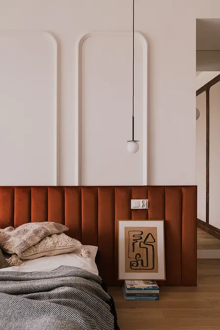 Sypialnia z wezgłowiem w stylu art deco i vintage, z książkami i nowoczesnym oświetleniem.