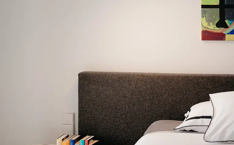 Wnętrze sypialni z szarym wezgłowiem, nowoczesnym oświetleniem i sztuką eklektyczną