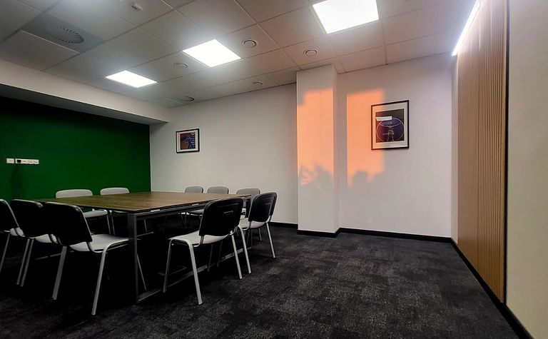Wnętrze sali konferencyjnej z zieloną ścianą, drewnianym stołem i krzesłami, nowoczesny design