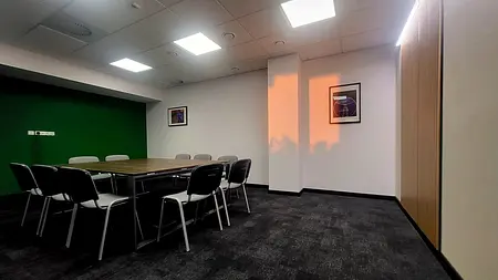 Wnętrze sali konferencyjnej z zieloną ścianą, drewnianym stołem i krzesłami, nowoczesny design