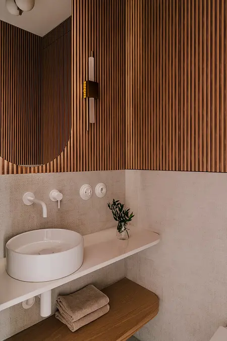 Wnętrze łazienki w stylu art deco i vintage z białą umywalką i drewnianymi detalami.