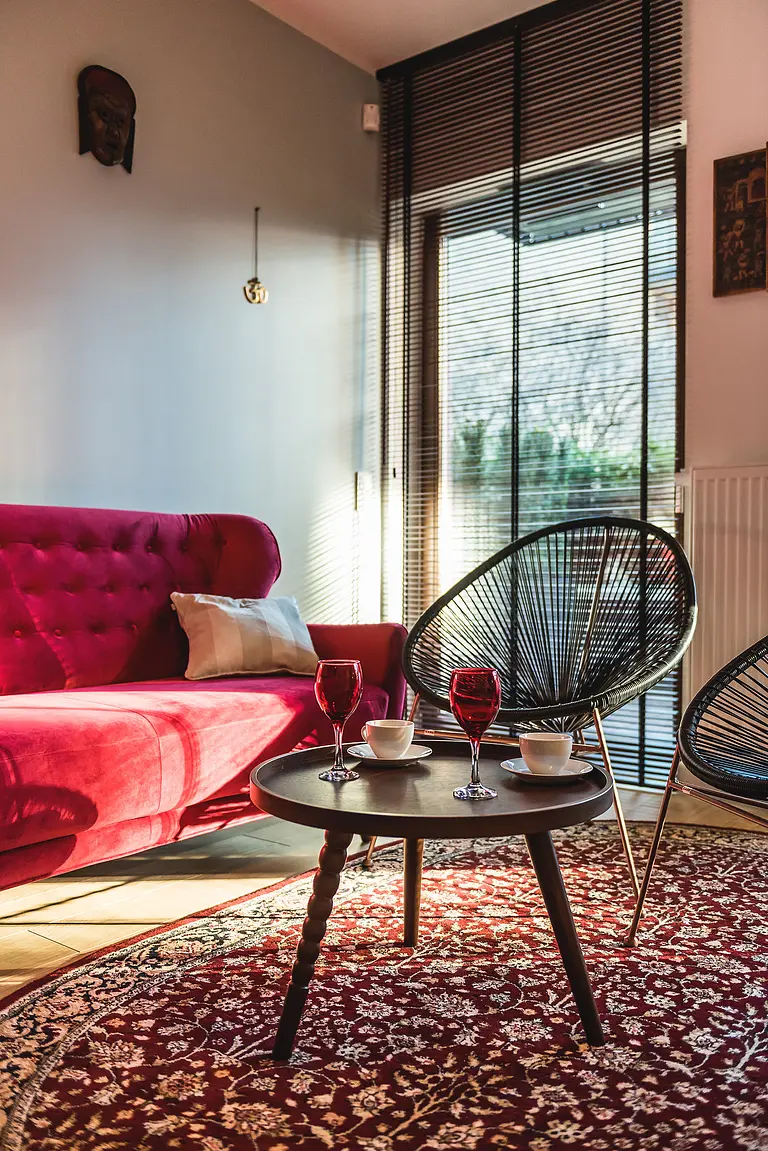 Wnętrze salonu z różową sofą, czarnymi fotelami i stołem kawowym w stylu eklektycznym.