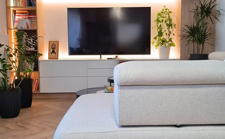 Wnętrze nowoczesnego salonu ze szarym narożnikiem i roślinami.