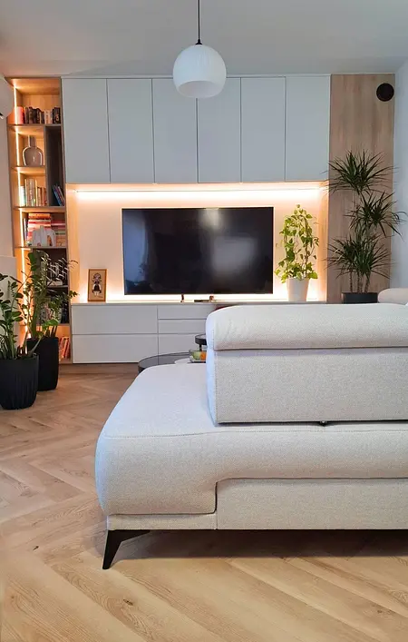 Wnętrze nowoczesnego salonu ze szarym narożnikiem i roślinami.