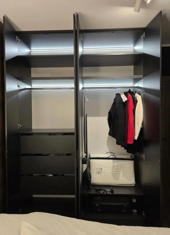Garderoba minimalistyczna z czarnymi szafkami i oświetleniem LED, z ubraniami i półkami.