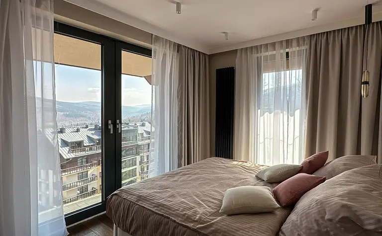 Sypialnia z dużym łóżkiem, poduszkami i zasłonami, nowoczesna aranżacja