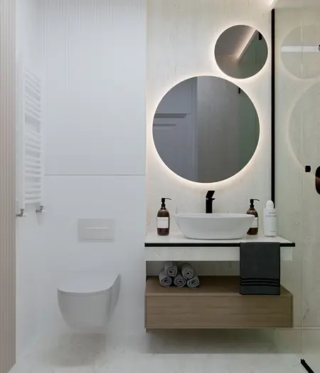 Wnętrze łazienki z okrągłym lustrem, minimalistycznymi meblami i detalami w stylu art deco i współczesnym.