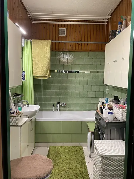 Mała łazienka z zielonymi płytkami, wanną i kosmetykami.