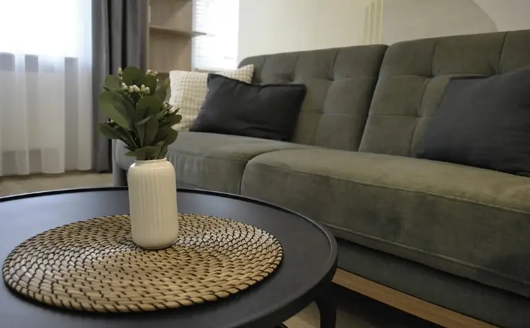 Wnętrze salonu w stylu minimalistycznym z zieloną sofą i czarnym stolikiem.