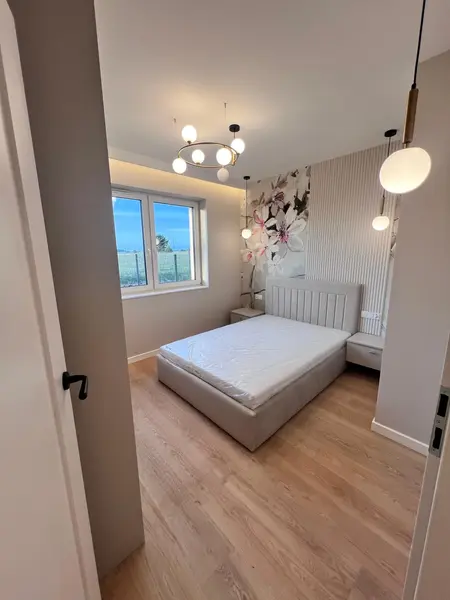 Sypialnia z jasnym łóżkiem, kwiatową ścianą i nowoczesnym oświetleniem w stylu glamour.