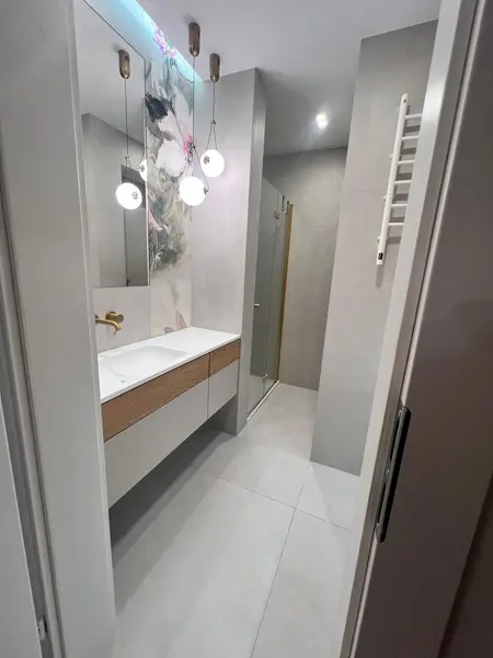 Nowoczesna łazienka z szarymi płytkami, drewnianymi elementami i oświetleniem glamour.