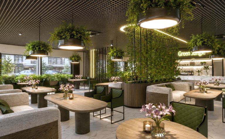 Wnętrze restauracji z roślinami, drewnianymi meblami i jasnymi dekoracjami.