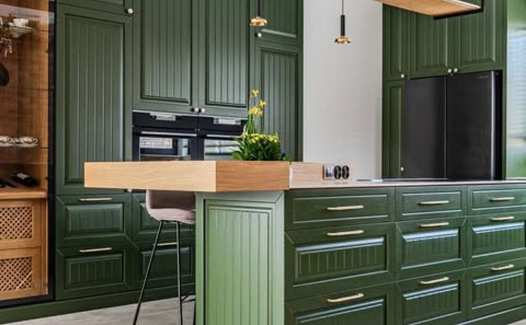 Kuchnia eklektyczna z zielonymi meblami i drewnianym blatem, roślinami w doniczkach.