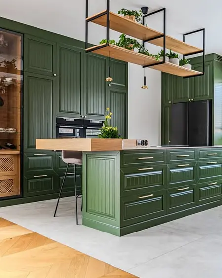 Kuchnia eklektyczna z zielonymi meblami i drewnianym blatem, roślinami w doniczkach.