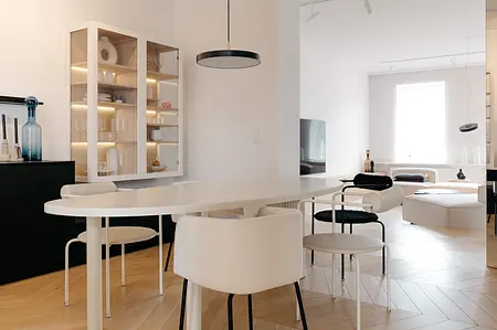 Wnętrze jadalni w stylu minimalistycznym z białym stołem, czarnymi krzesłami i drewnianą podłogą.