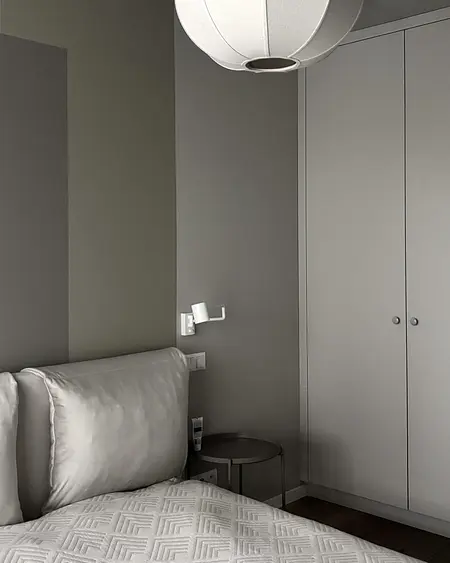 Sypialnia w stylu minimalistycznym z szarymi ścianami, białymi meblami i lampą.