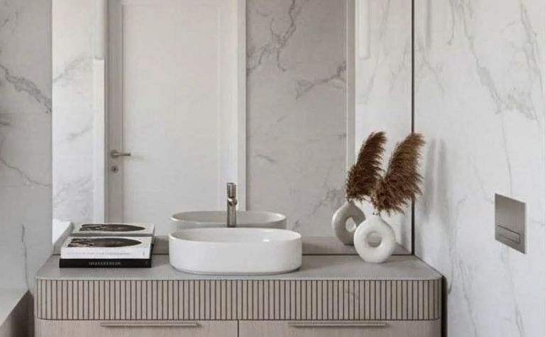 Nowoczesna łazienka z białą umywalką, drewnianymi szafkami i marmurowymi ścianami, minimalistyczny styl