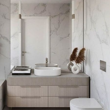 Nowoczesna łazienka z białą umywalką, drewnianymi szafkami i marmurowymi ścianami, minimalistyczny styl