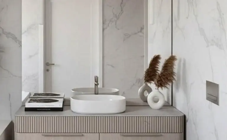 Nowoczesna łazienka z białą umywalką, drewnianymi szafkami i marmurowymi ścianami, minimalistyczny styl