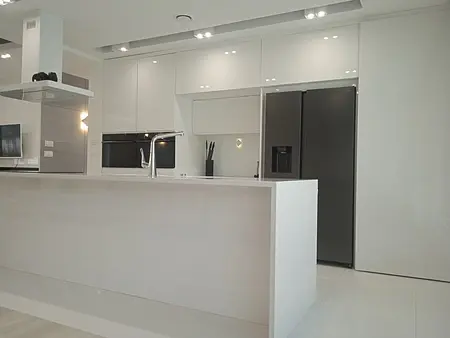 Nowoczesna kuchnia minimalistyczna z białymi meblami i czarnym sprzętem.