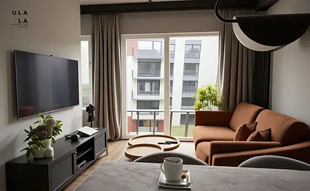 Wnętrze salonu z brązową sofą, telewizorem i rośliną