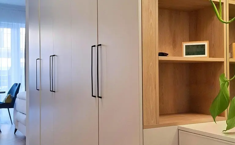 Garderoba z białymi meblami, drewnianymi półkami i rośliną