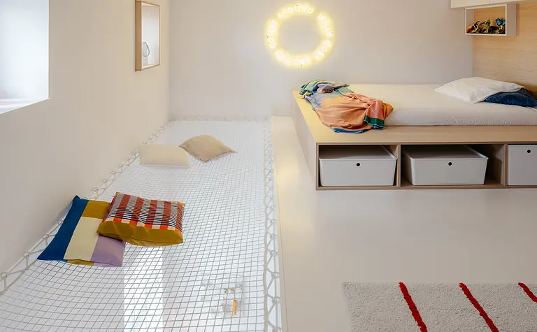 Wnętrze pokoju w stylu eklektycznym z minimalistycznym łóżkiem i kolorowymi poduszkami.